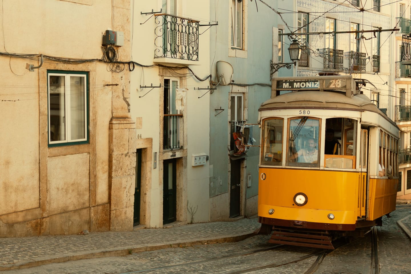 Yellow tram climbing towards an Alfama miradouro.