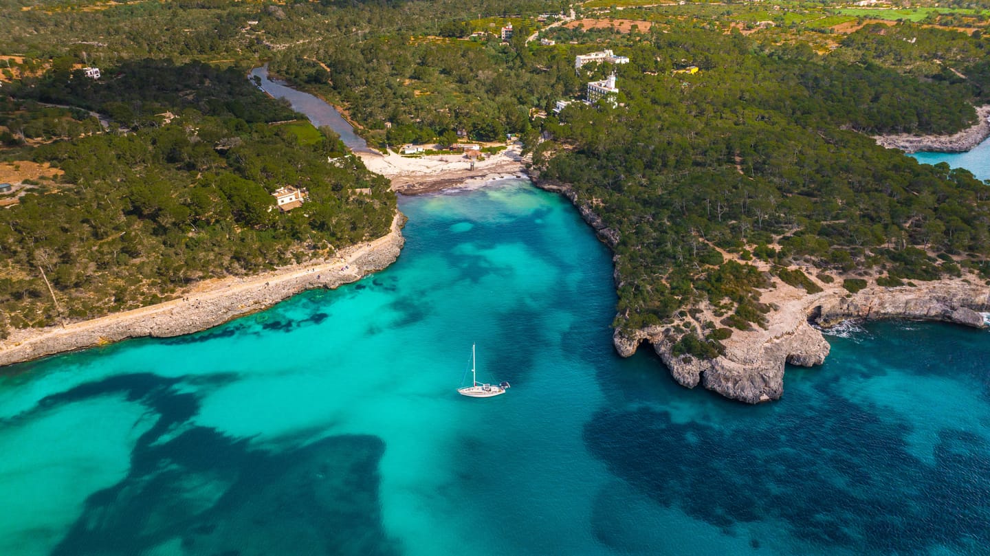 Crique turquoise bordée de pins, voiliers au mouillage.