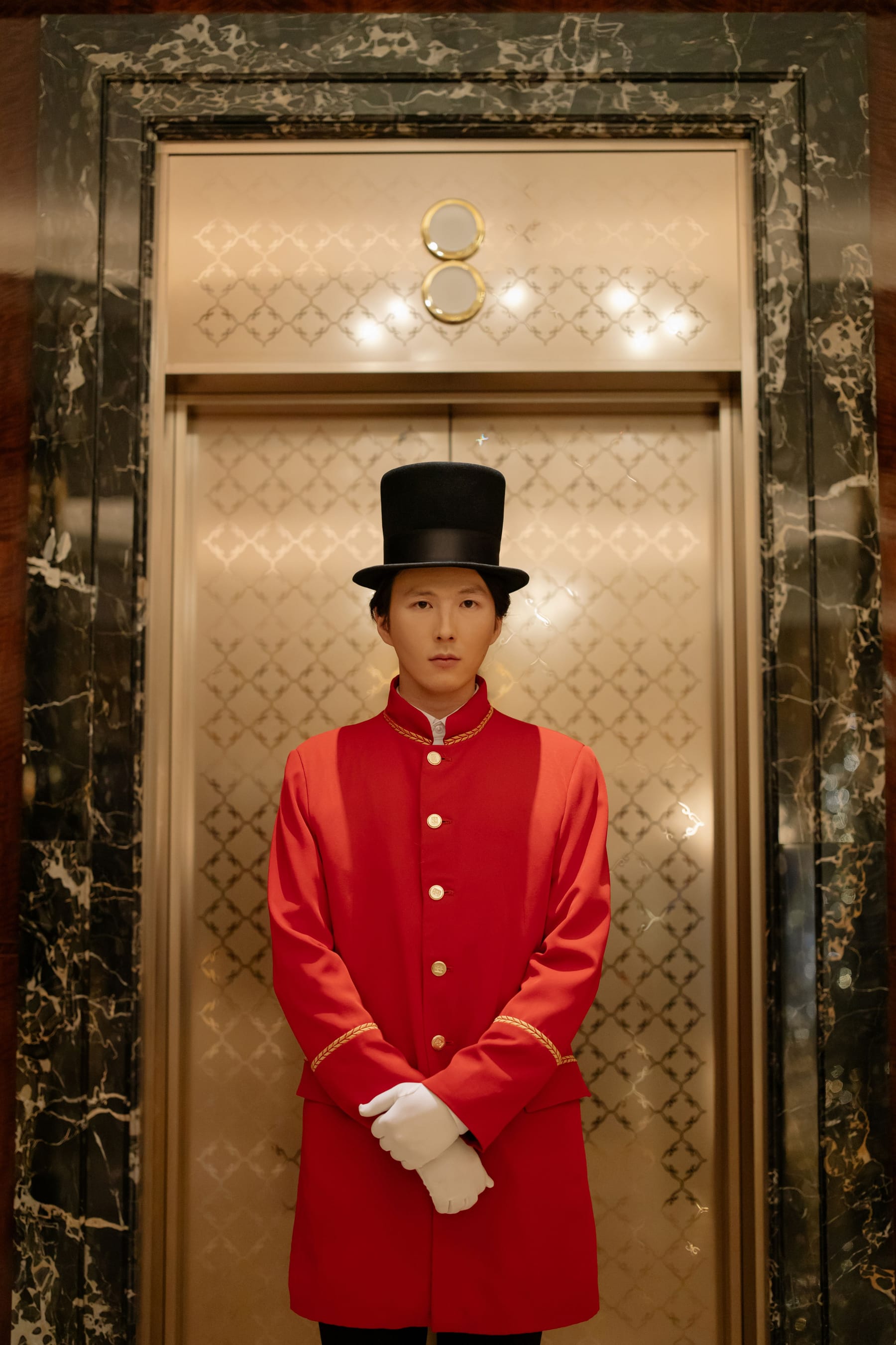 Un chasseur en uniforme devant l'ascenseur d'un palace.